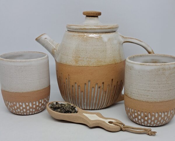 Théière blanc brillant, tasses assorties et cuillère doseuse pour le thé.